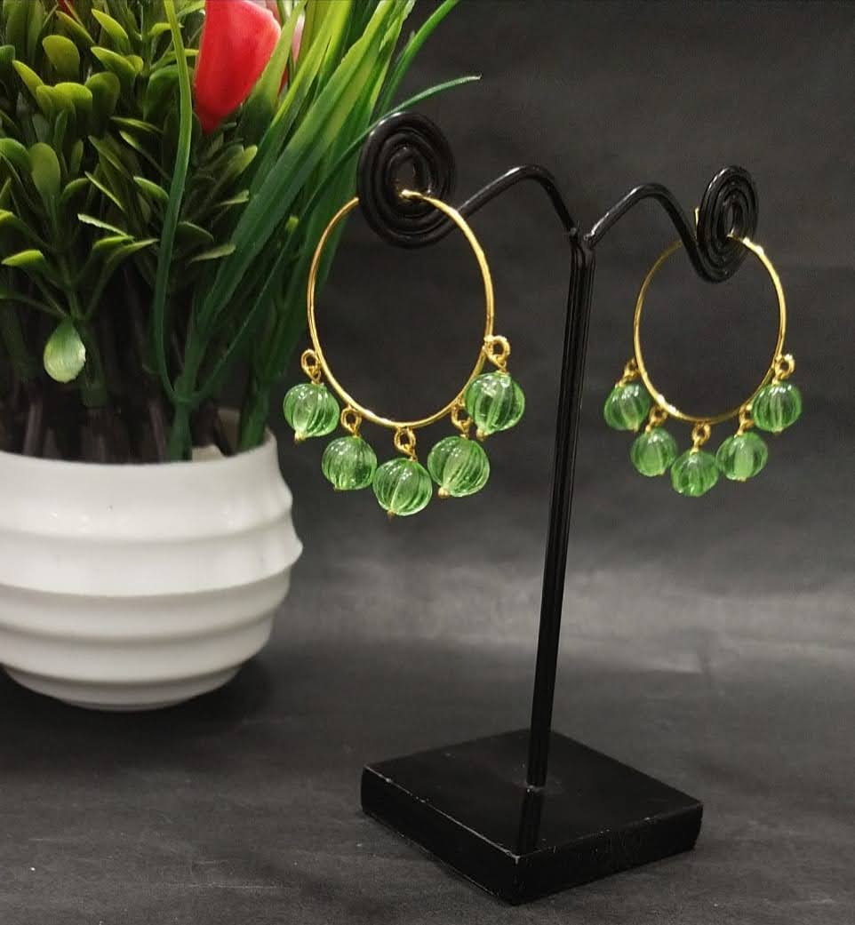 Green crystal bead drop earrings displayed on a black jewelry stand with a potted plant in the background.