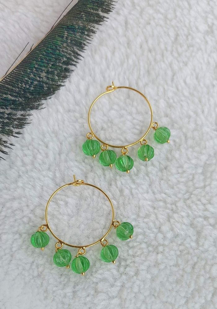 Green beaded earrings on a soft, plush white surface with a green fabric in the background.