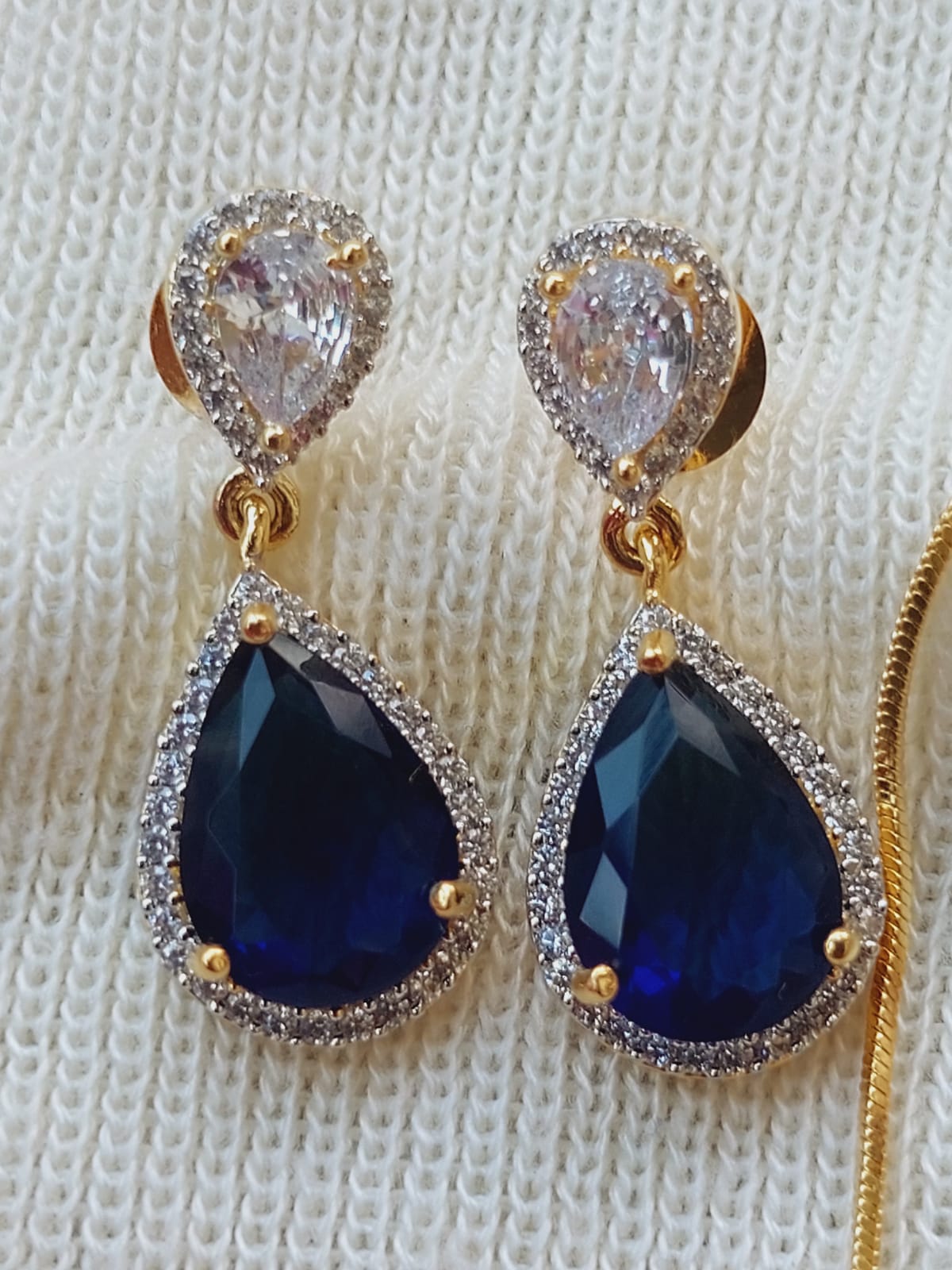 Dark Purple Glass Stone Contemporary Earrings
These elegant earrings feature striking teardrop-shaped dark purple glass stones surrounded by a halo of sparkling rhinestones, creating a contemporary and glamorous look. The earrings are displayed on a white knitted surface, showcasing their intricate design and luxurious appeal.