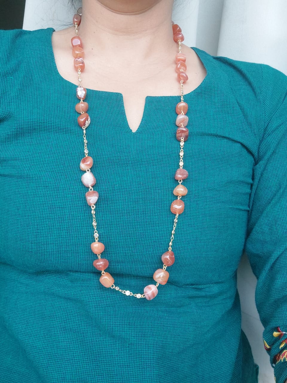 Orange glass beads and American diamond set necklace around a woman's neck against a turquoise blouse