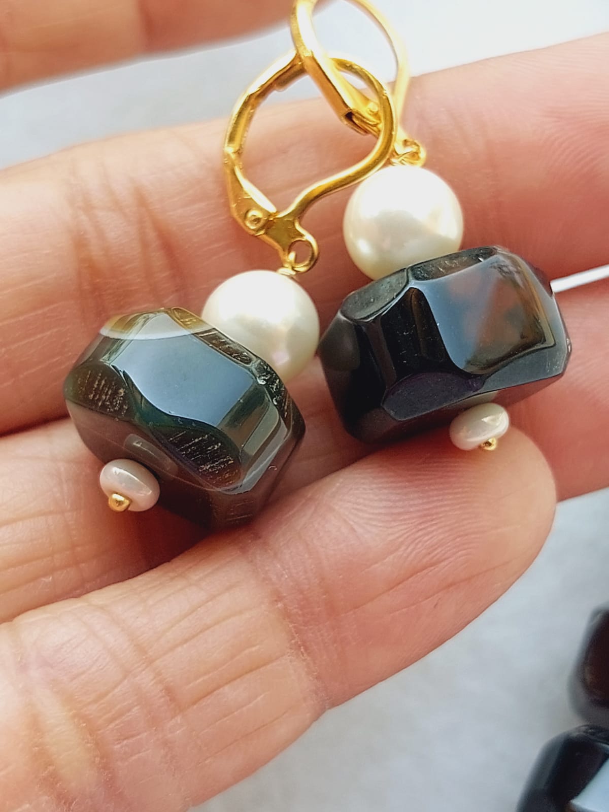 Elegant gold-toned earrings featuring natural black stones and lustrous pearls, showcased on a hand.
