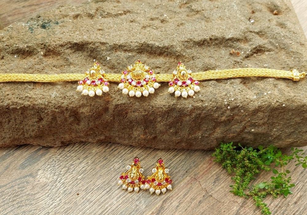 Elegant pearl and ruby studded golden bajuband and choker set from Mugdha Jewellery Store, artfully displayed on a rustic wooden surface.