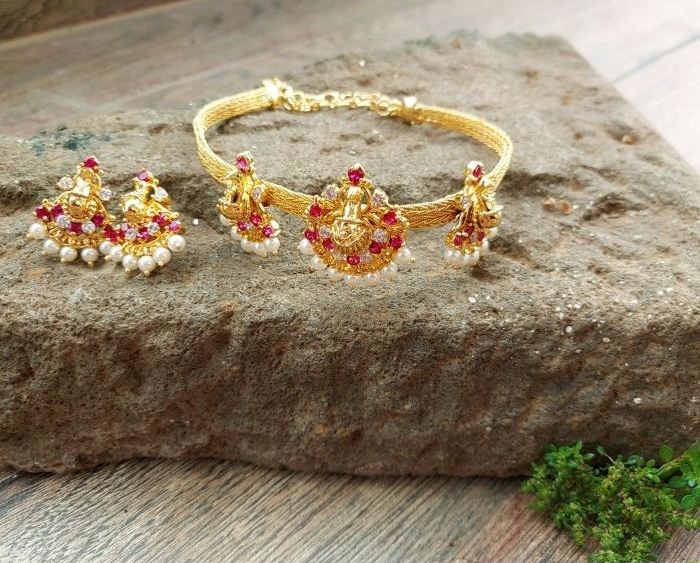 Elegant two-in-one gold-toned peacock bajuband and choker set with intricate ruby-colored gemstone accents, displayed on a rustic stone surface.