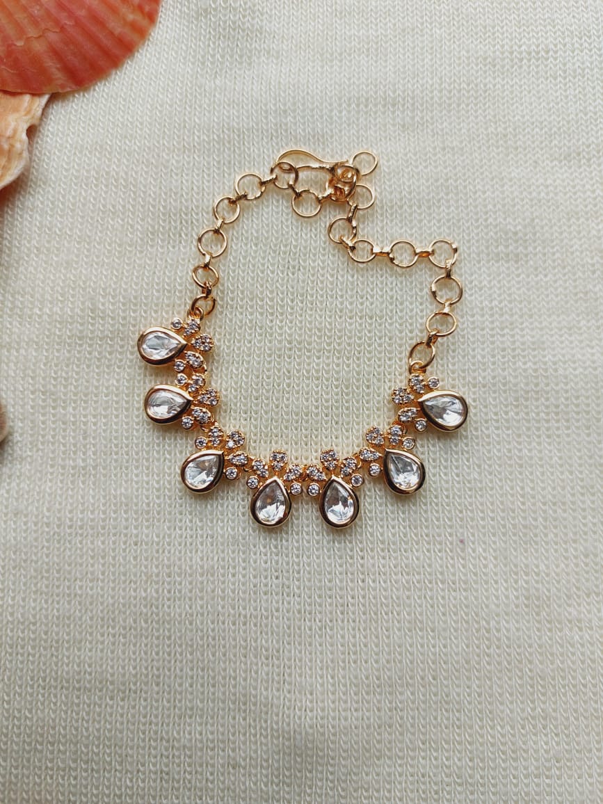 Elegant gold-toned leaf-shaped bracelet adorned with sparkling crystals, showcased on a light fabric background.