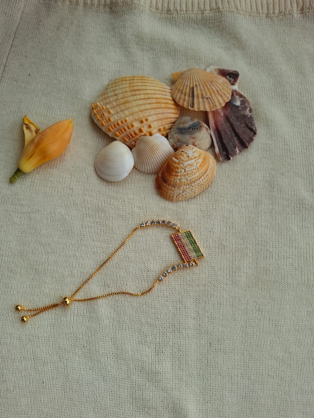 Elegant seashell jewelry design - gold and gemstone bracelet displayed with assorted seashells against a beige fabric background in Mugdha Jewellery Store