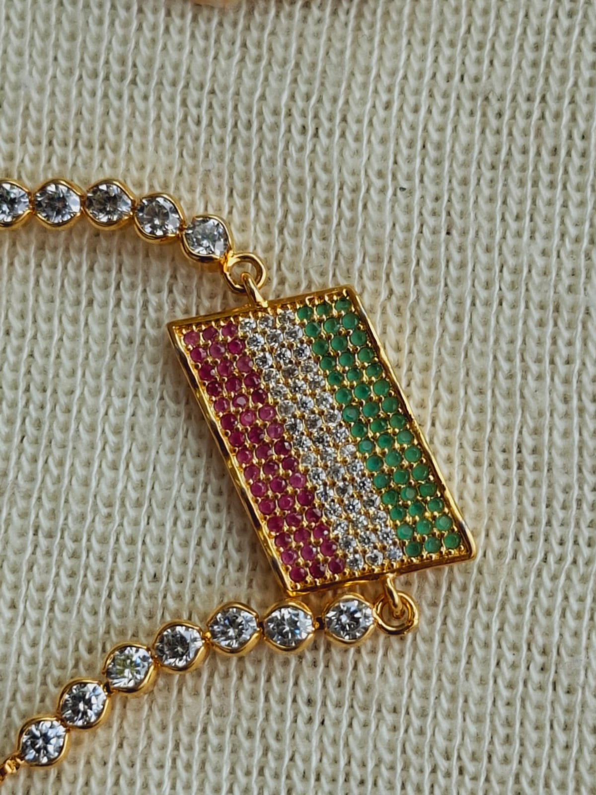 Golden designer bracelet with colorful gemstone accents displayed on a knitted fabric background.