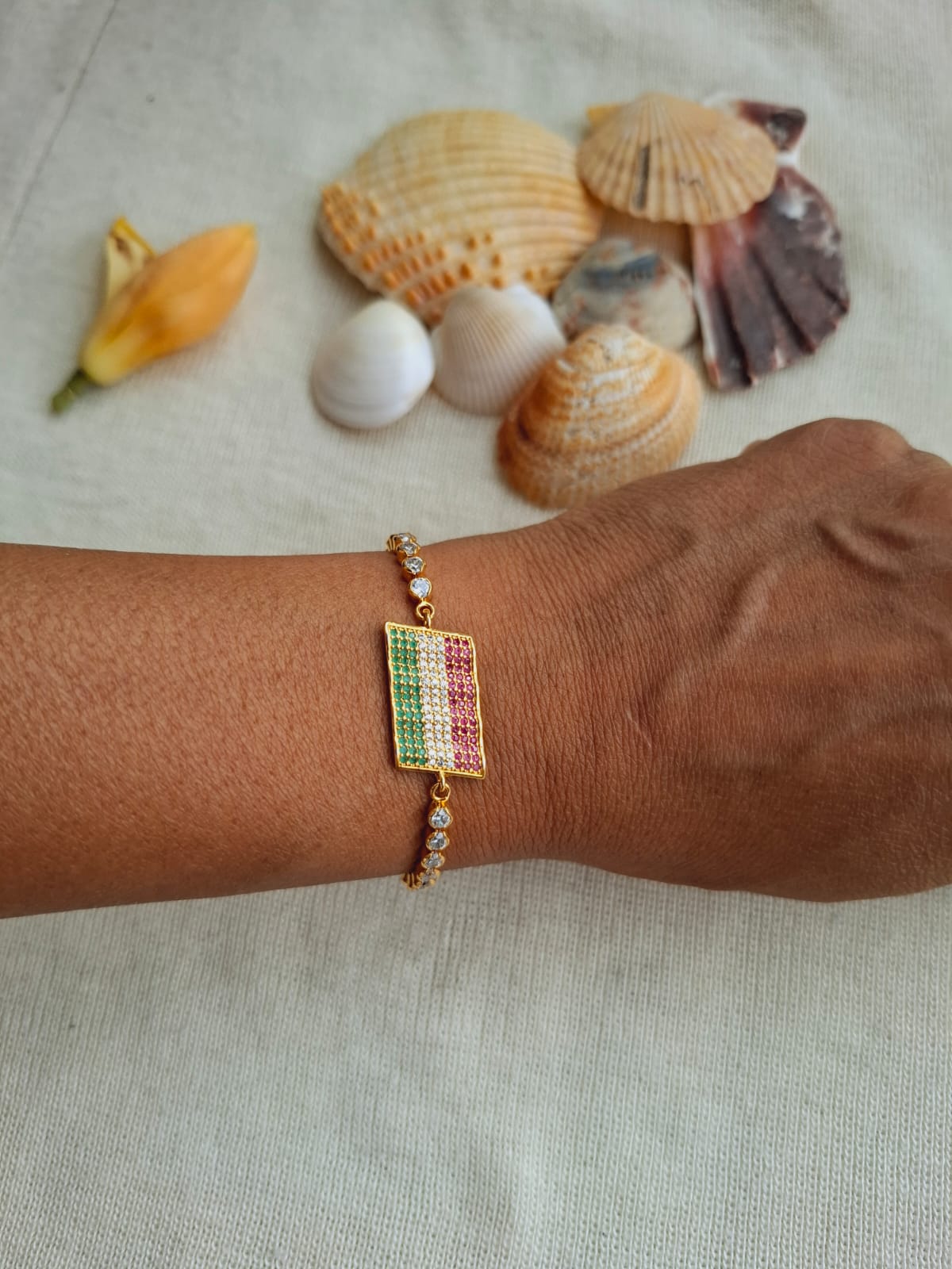 Vibrant gold and gemstone bracelet on a person's wrist, surrounded by seashells on a light background.