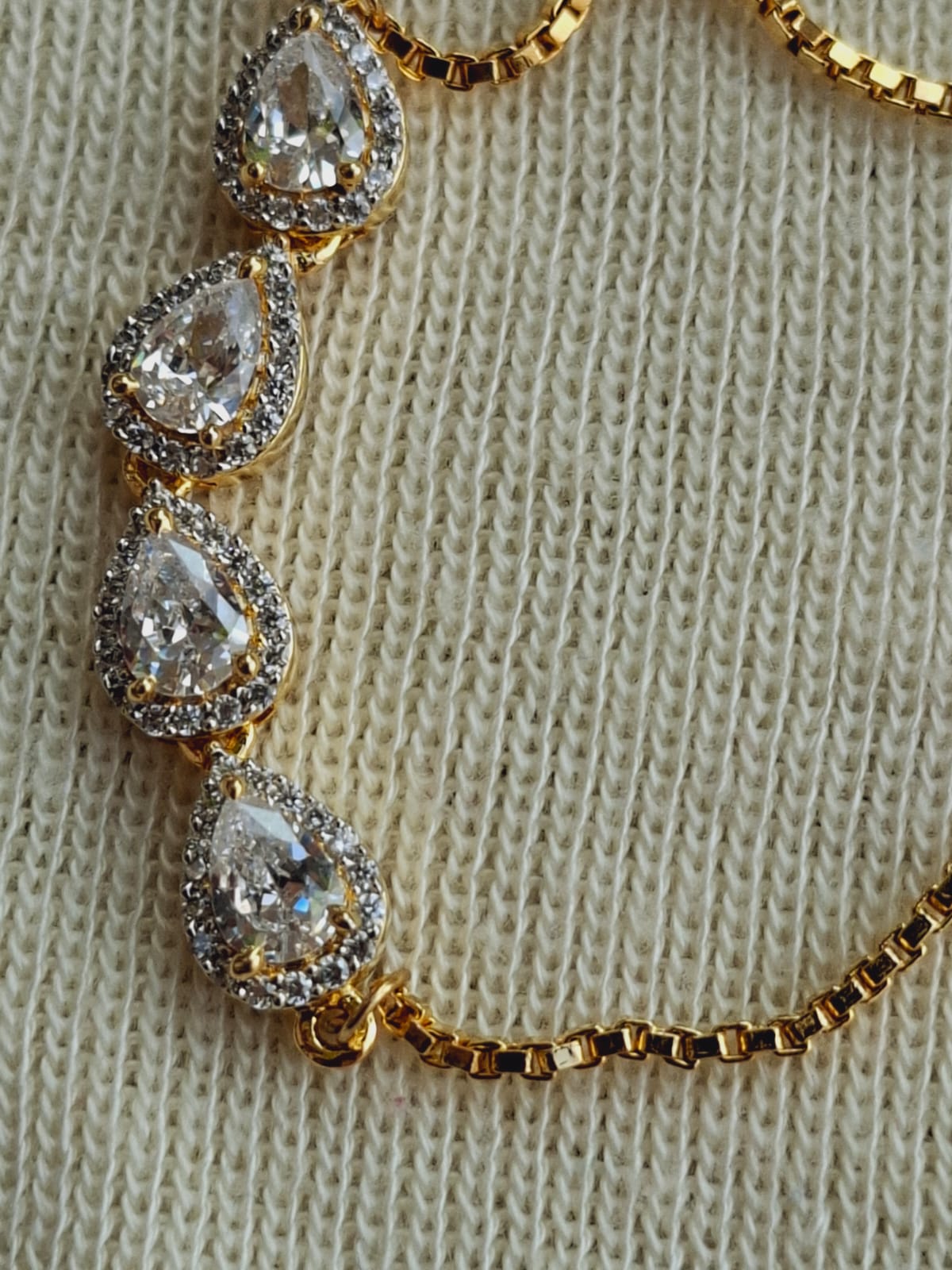 Elegant golden bracelet adorned with sparkling teardrop-shaped crystals, set against a cozy knitted background.