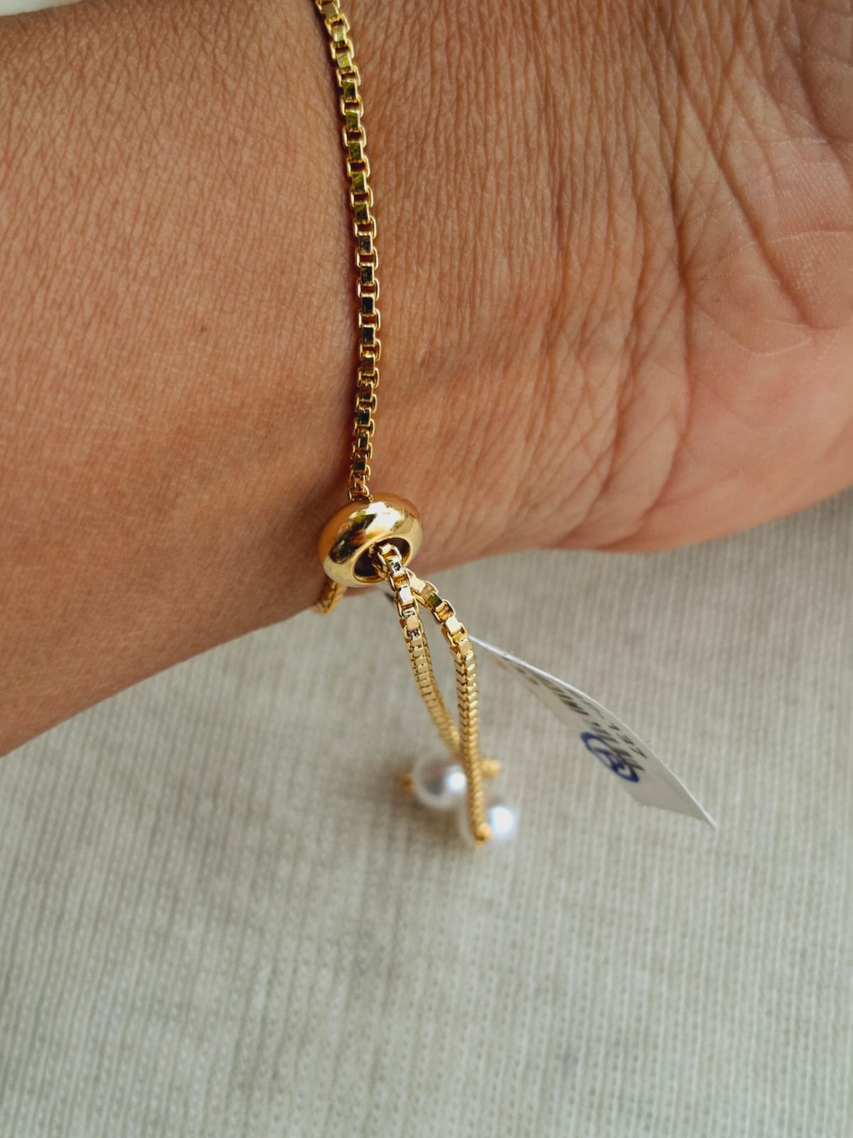 Elegant Golden Badam Bracelet with Sparkling Pearl Charm - Showcased on a person's wrist, the adjustable golden bracelet features a delicate badam (almond) shape design accented with a shimmering pearl charm, creating a chic and refined accessory.
