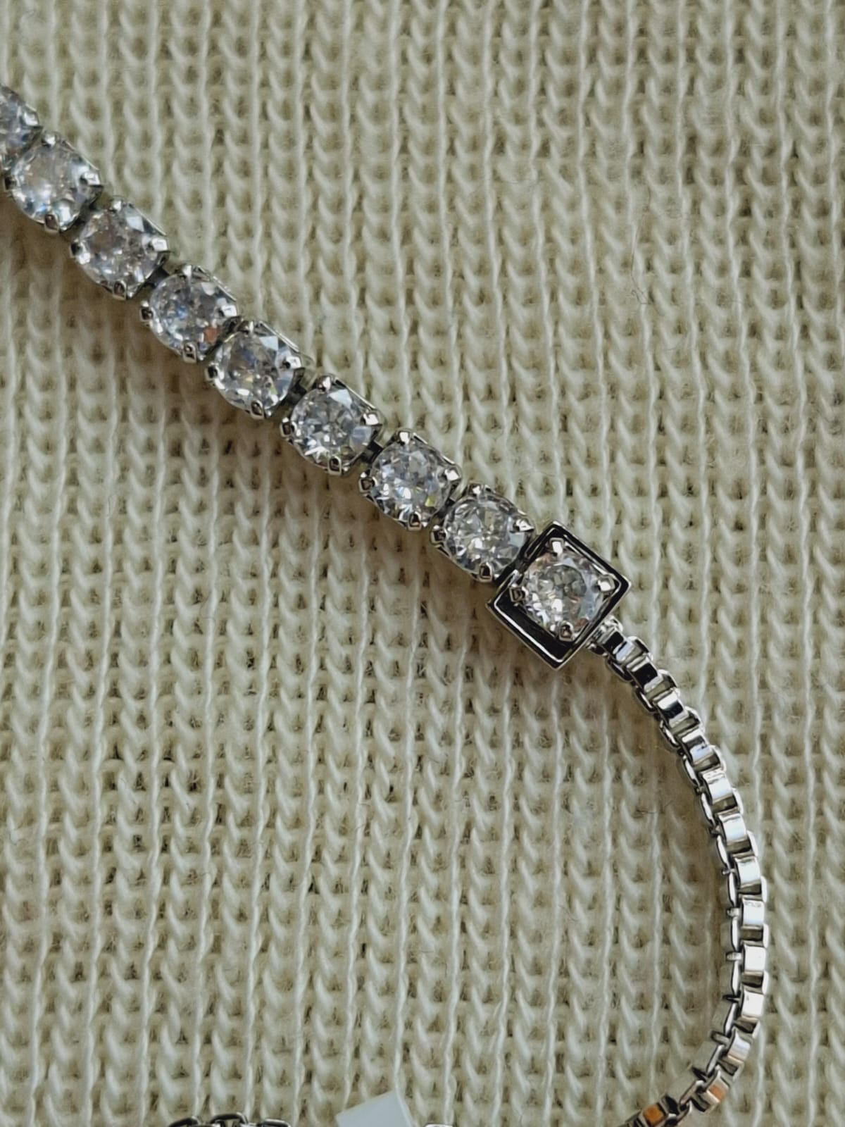 High quality silver adjustable bracelet with sparkling American diamonds set in a row, placed on a textured off-white knitted background.