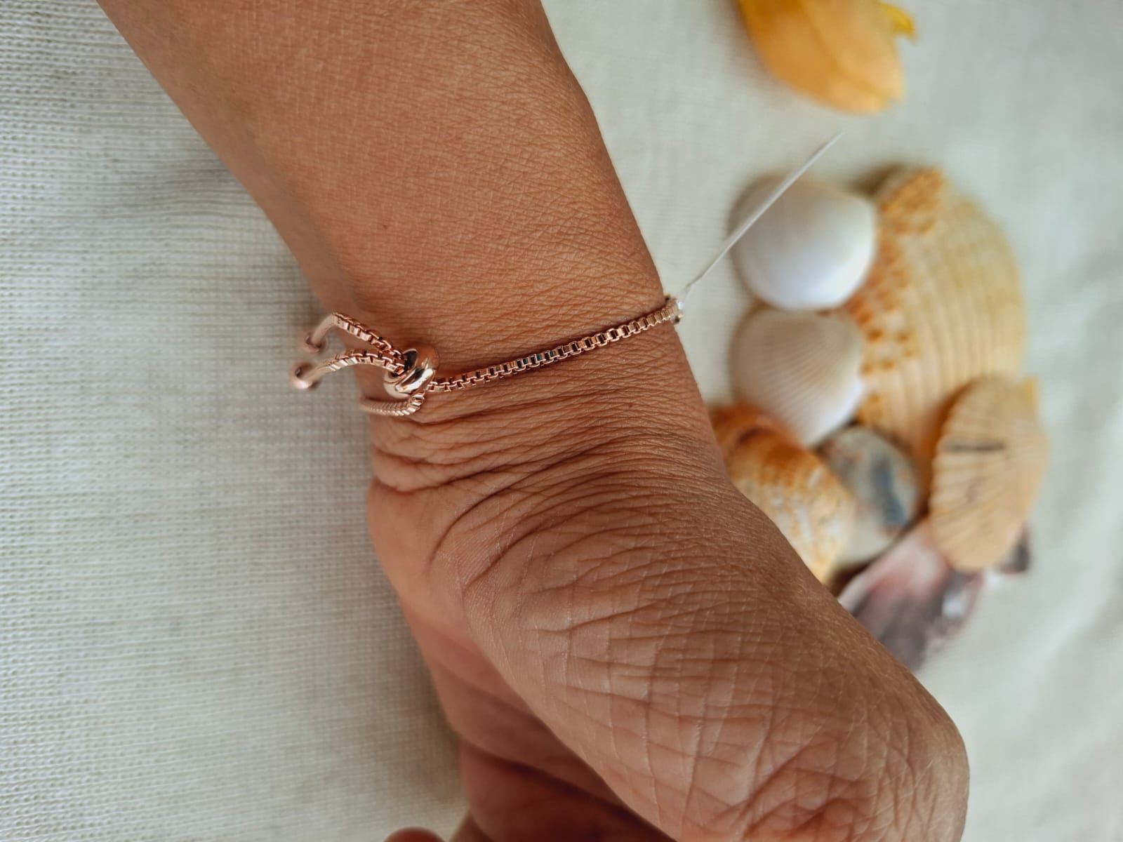 High-quality American diamond rose gold adjustable bracelet on a person's wrist, with seashells in the background.