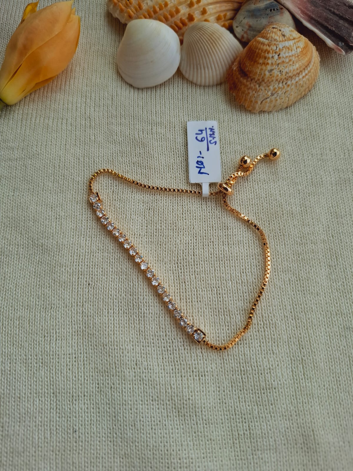 Elegant American diamond gold-tone adjustable bracelet displayed on natural fabric with seashells.
