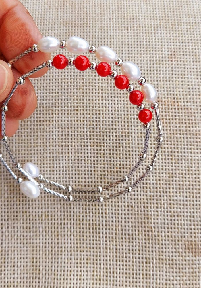 Elegant pearl and coral designer bracelet displayed on a hand against a neutral fabric background