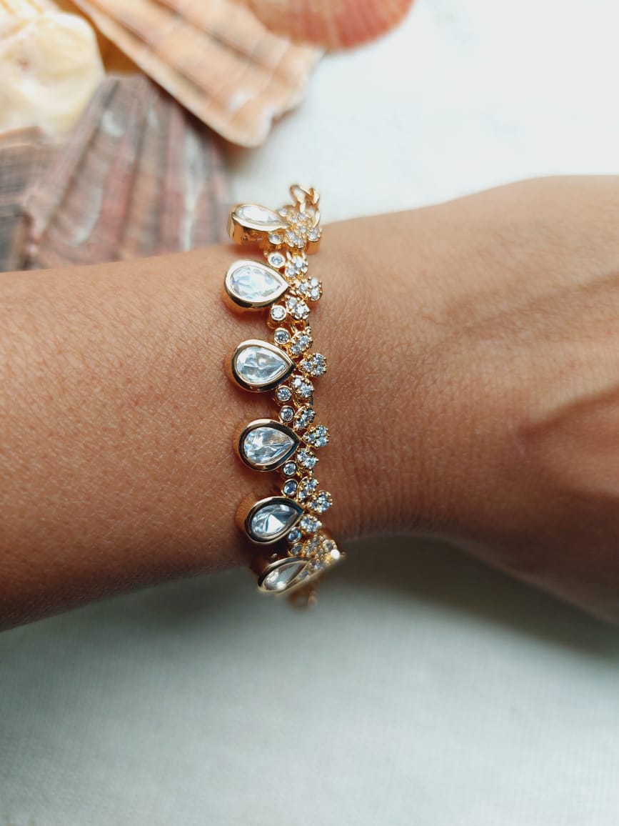 Elegant gold-tone leaf-shaped bracelet with sparkling crystal accents, displayed on a female wrist against a blurred background.