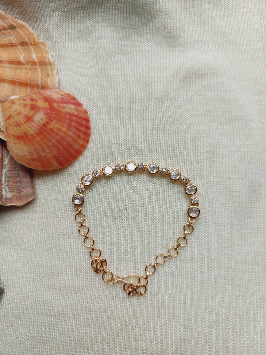 Elegant Kundan Bracelet - Decorative golden-toned bracelet with round kundan gemstones, placed on a textured light background with seashells.