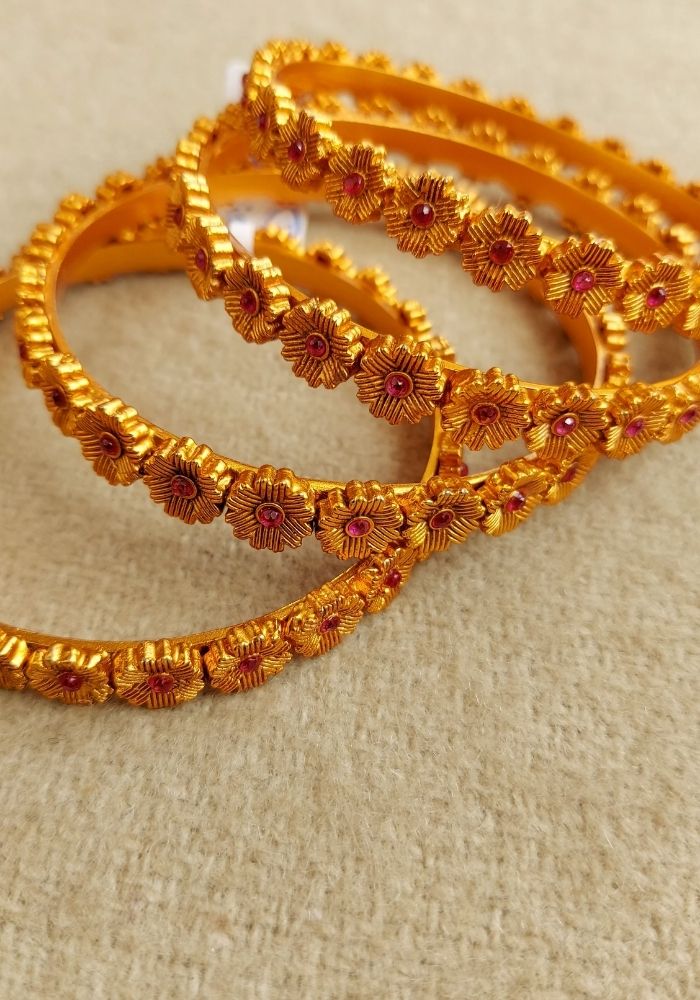 Elegant gold temple bangles with intricate floral patterns, displayed on a neutral background at the Mugdha Jewellery Store.