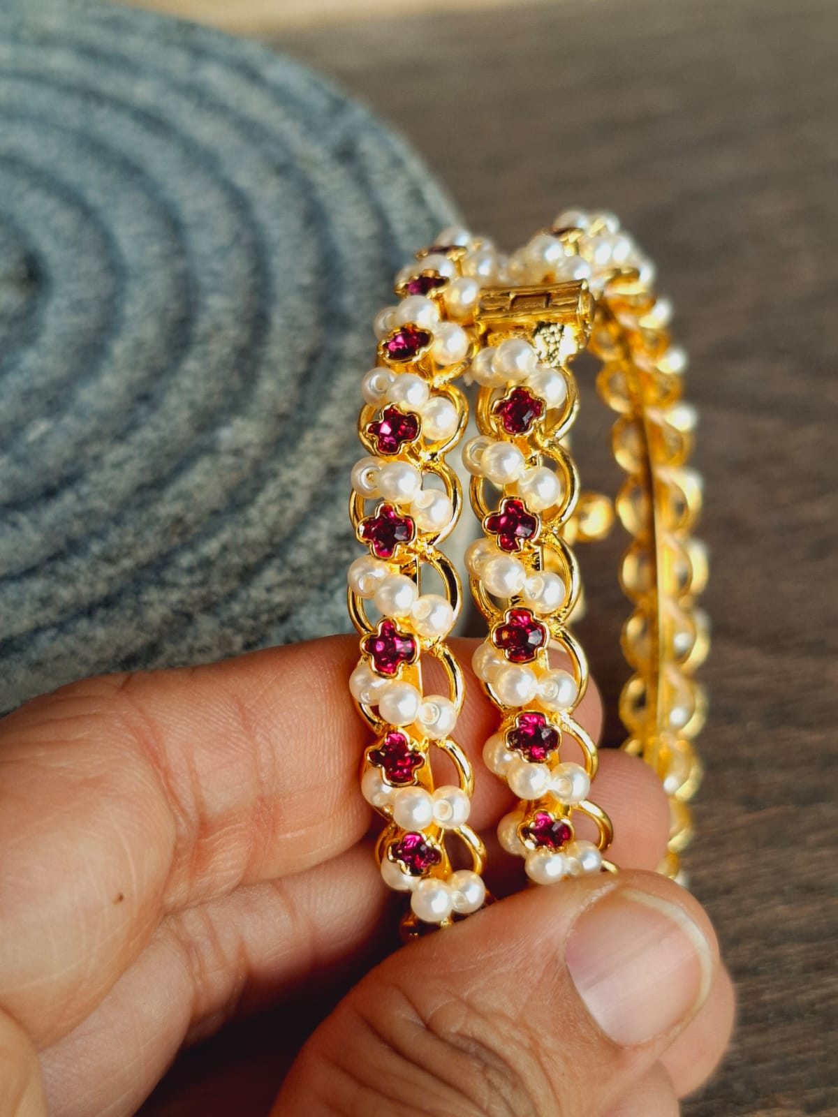 Gold-tone bangles with red gemstones and pearls on a textured background