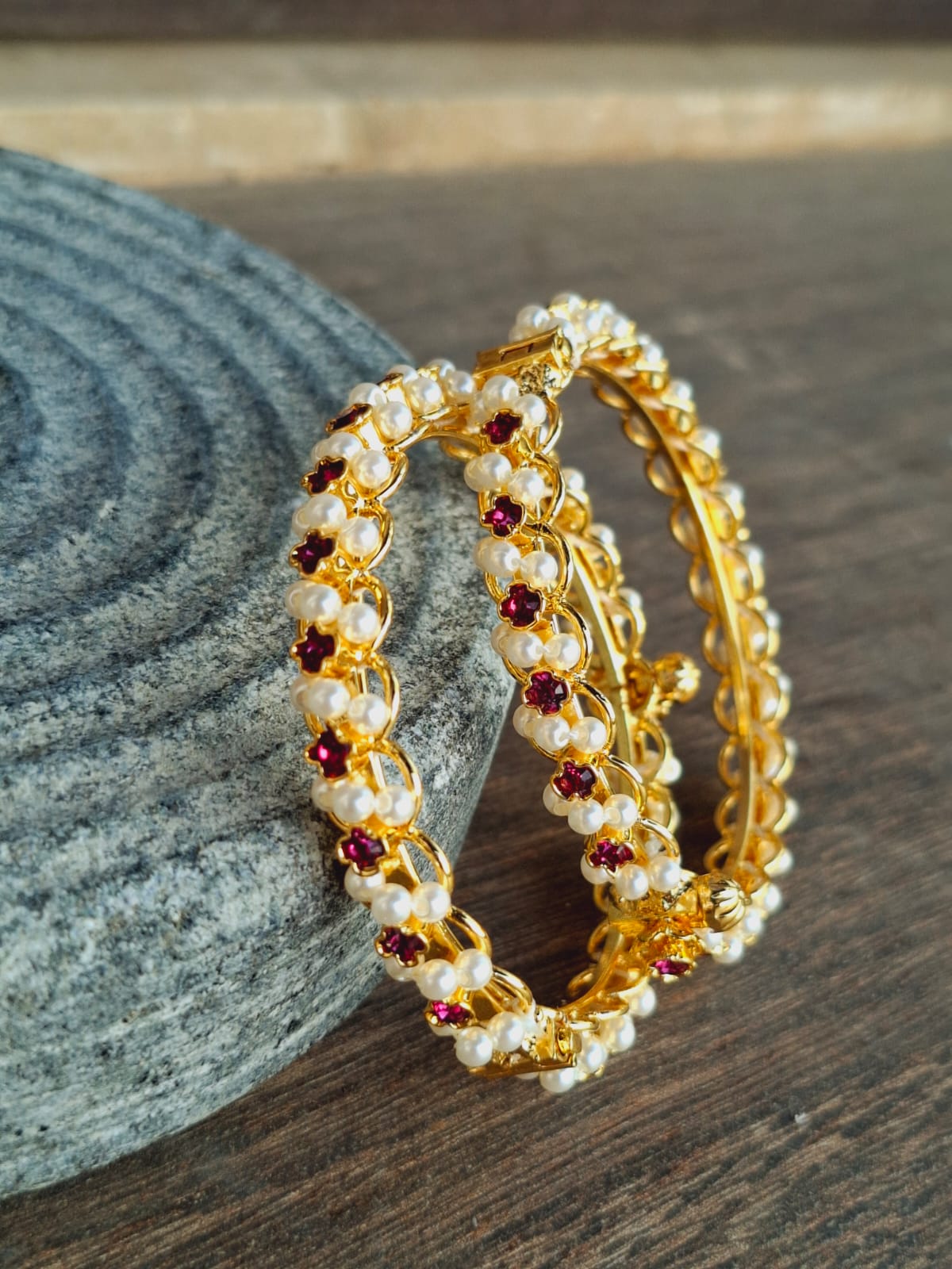 Elegant gold-tone bangles with pearl and ruby accents from Mugdha Jewellery Store. The intricate floral design adds a touch of refined sophistication to the jewellery piece.