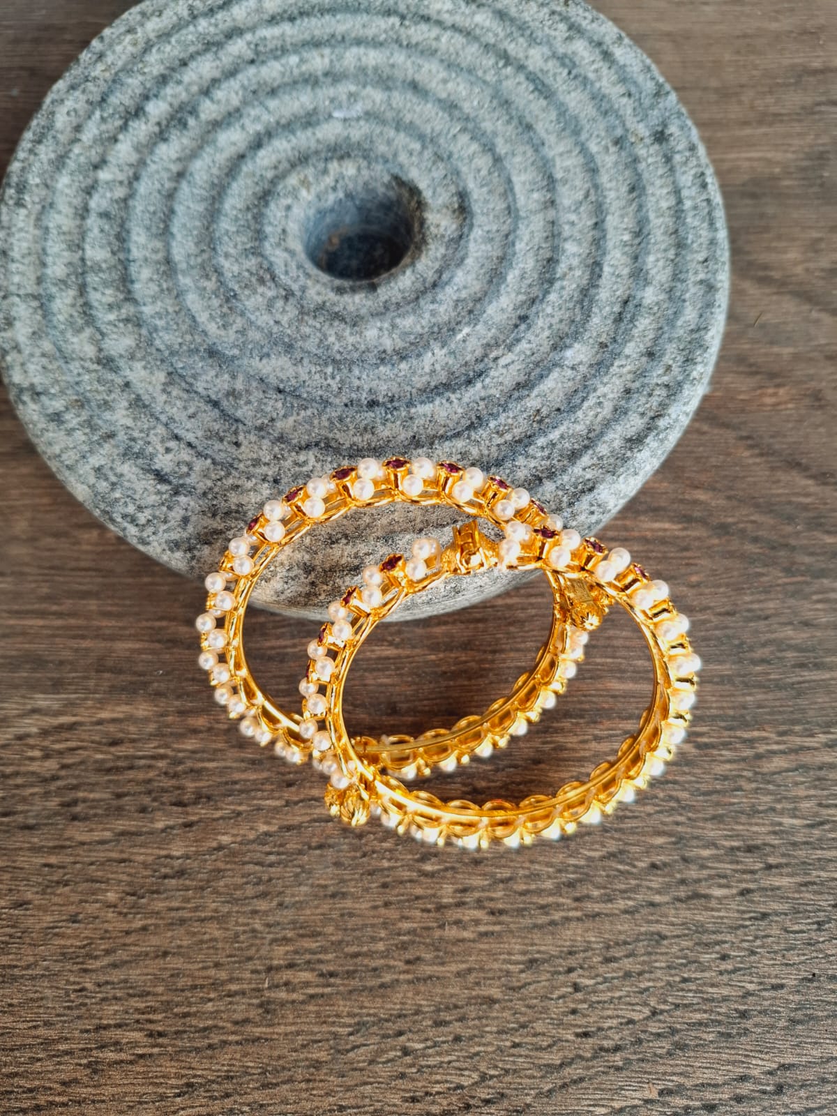 Elegant gold-tone bangles with sparkling gemstones, set against a textured gray backdrop.