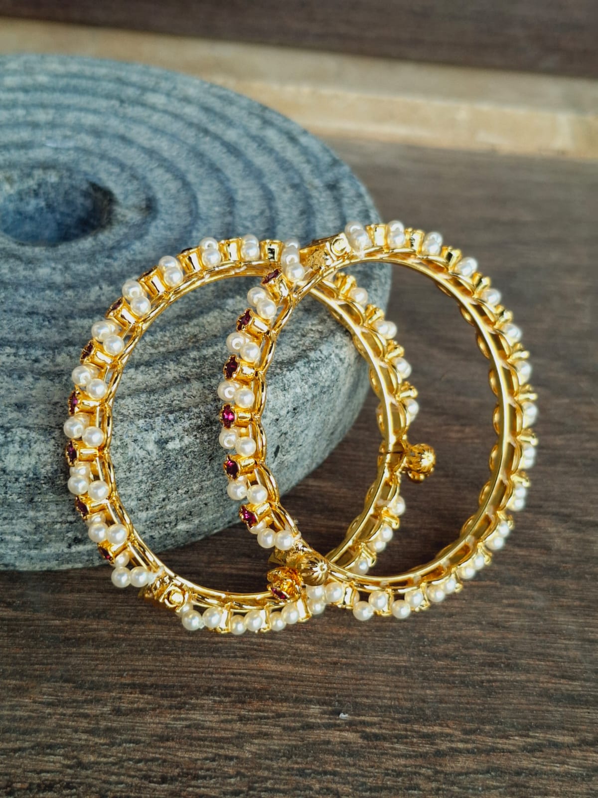 Elegant gold-tone bangles with sparkling rhinestones, displayed on a gray textured surface.