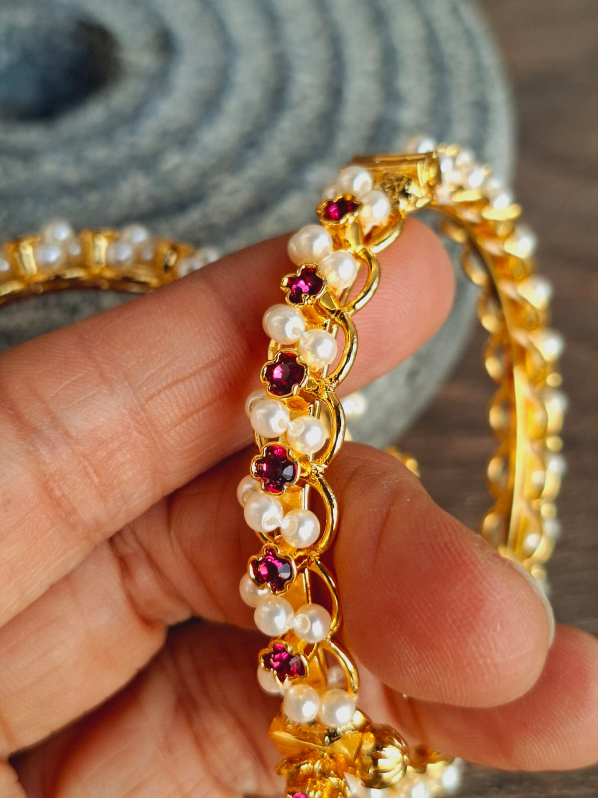 Intricate gold chain with pearl and ruby accents. Ornate jewelry piece displayed against a textured gray fabric backdrop.