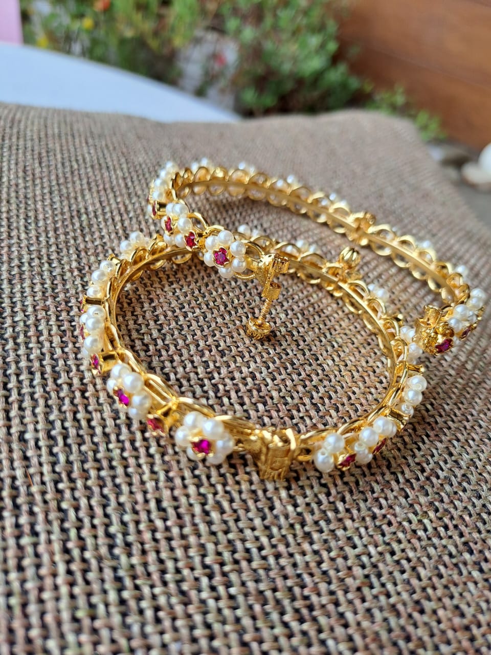 Ornate gold-toned bangle bracelets adorned with colorful gemstones, displayed on a textured fabric surface.