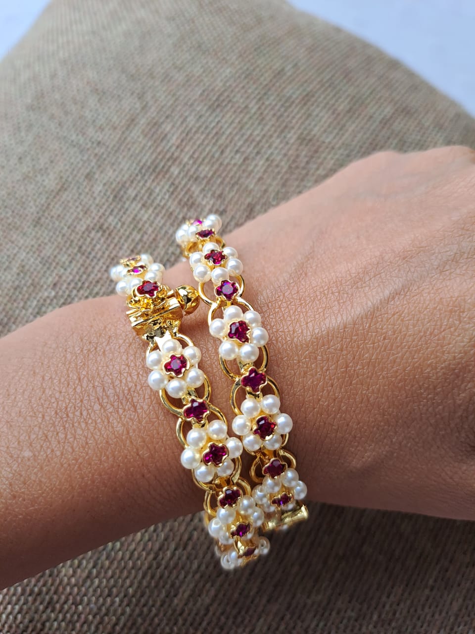 Traditional Kudi Tode. Set of 2. Gold-toned floral bracelets with red gemstones and white pearls on a textured background.