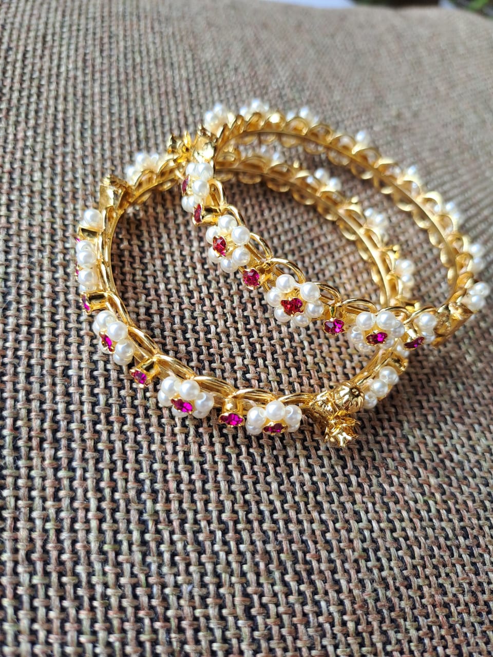 Elegant gold-tone bangles adorned with sparkling crystals, displayed on a textured fabric surface.