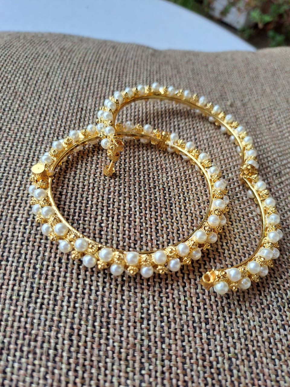 Traditional Gopi Tode. Set of 2 golden hooped earrings adorned with pearls, displayed on a textured fabric background.