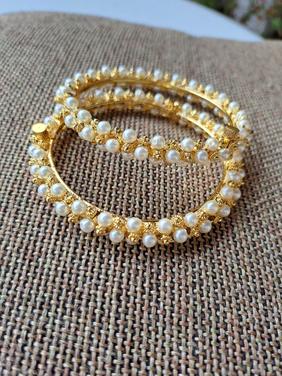 Elegant gold and pearl bangles on textured fabric background