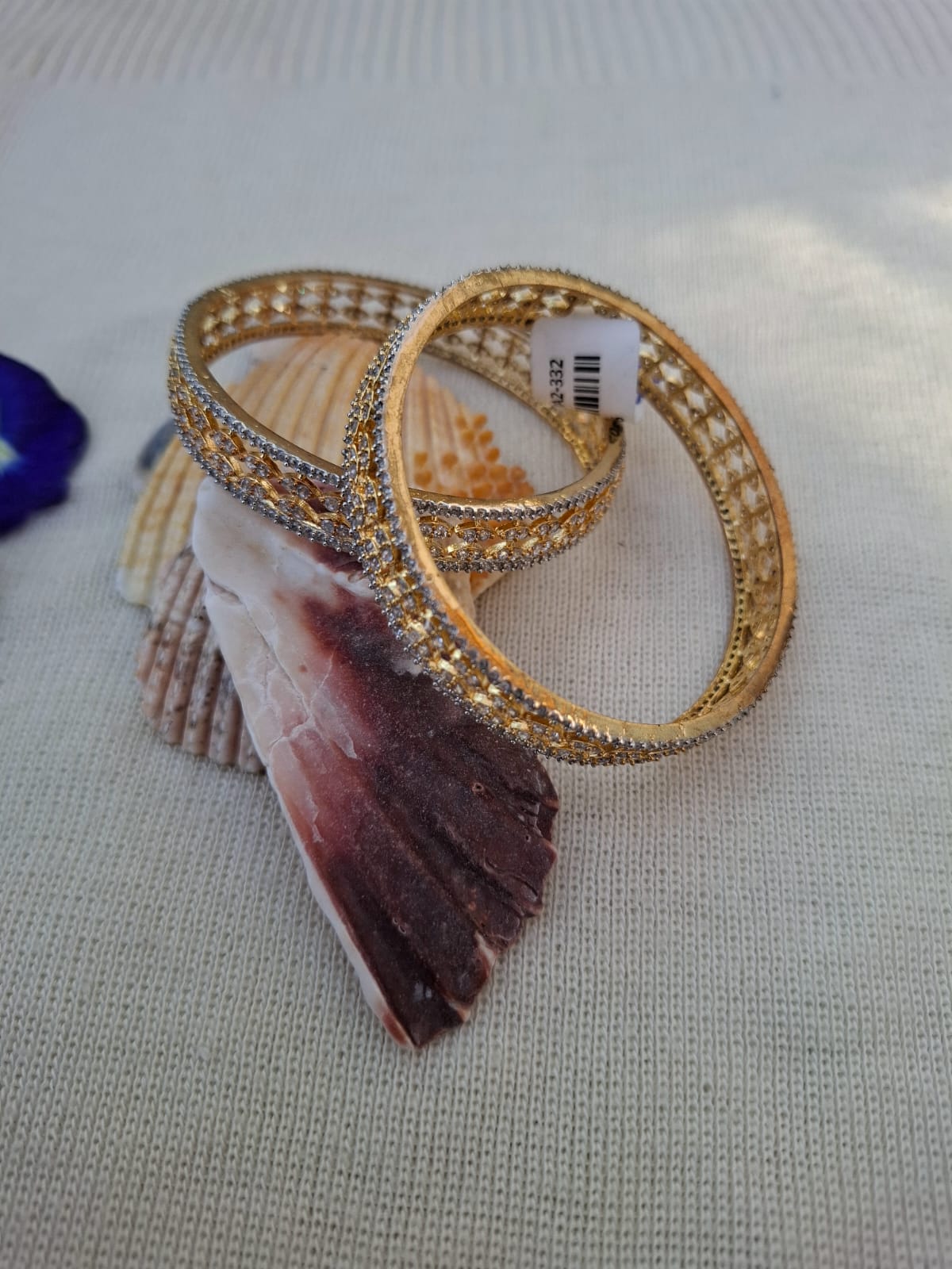 Pair of sparkling golden American diamond designer bangles with intricate encrusted patterns, set against a purple gemstone backdrop.