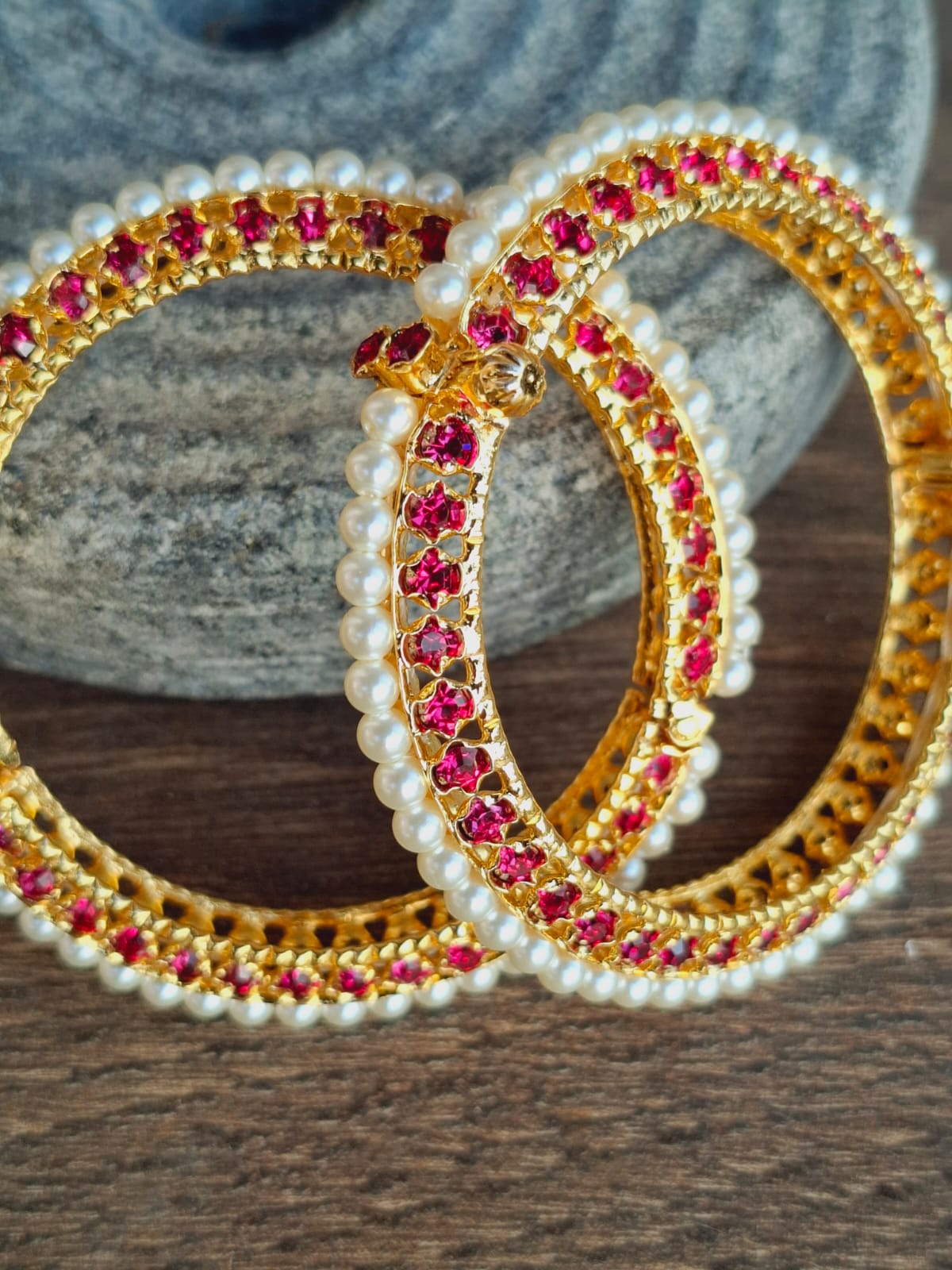 Ornate gold-toned hooped earrings adorned with pearls and vibrant fuchsia gemstones, placed on a textured grey surface.