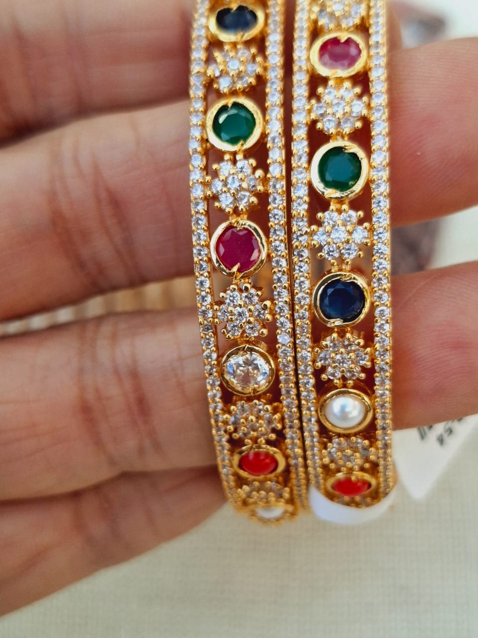 Elegant gold bracelets with colorful gemstones and sparkling diamond-like accents, showcased on a hand