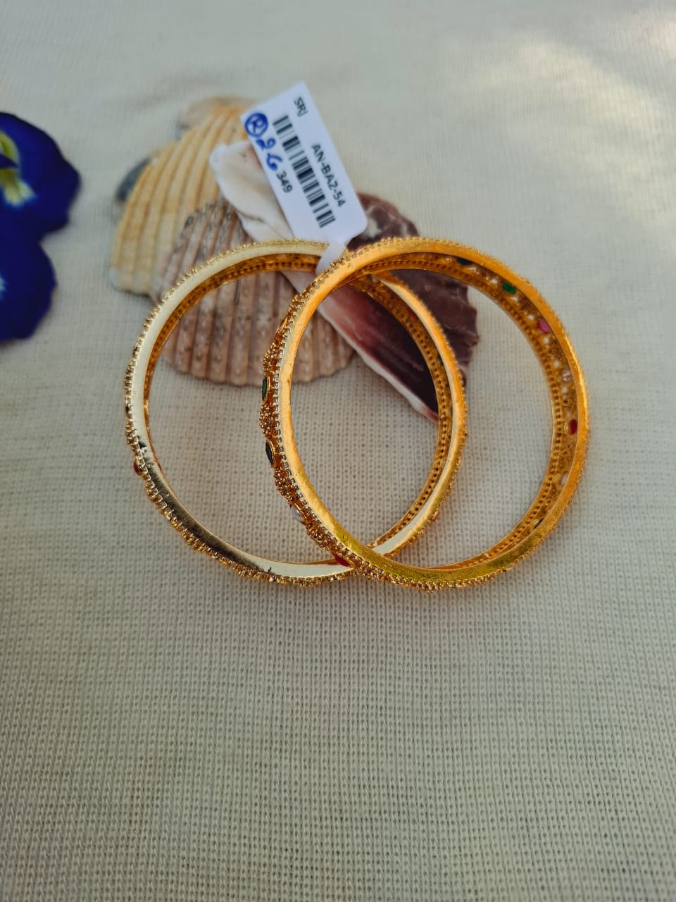 Pair of ornate golden bangles with decorative patterns, displayed on a textured light surface with price tag.