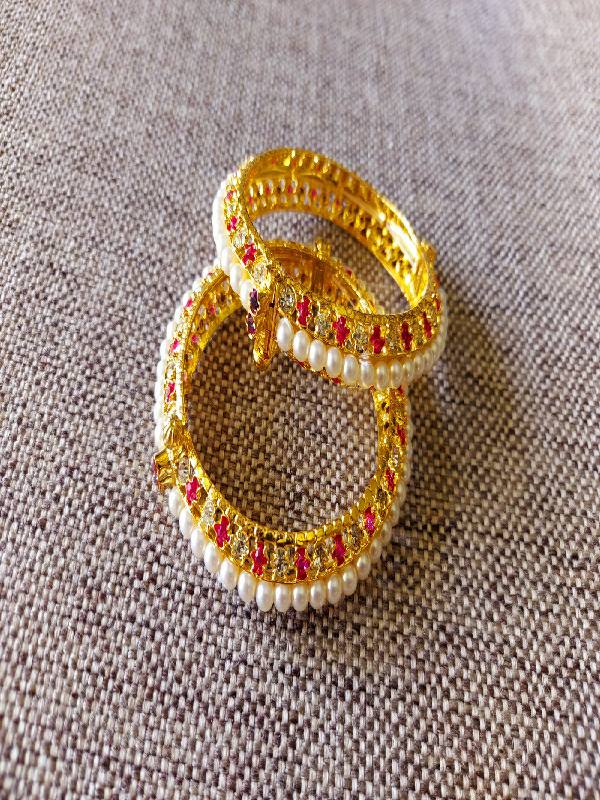 Traditional pearl tode bangles in dark pink and white colors, featuring intricate gold-toned embellishments. Set of 2 graceful bracelets displayed against a grey textured background.