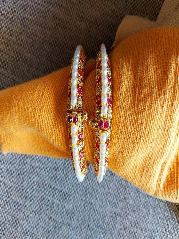 Elegant gold-toned traditional pearl tode jewelry with dark pink and white accents, showcased on a cozy fabric backdrop.