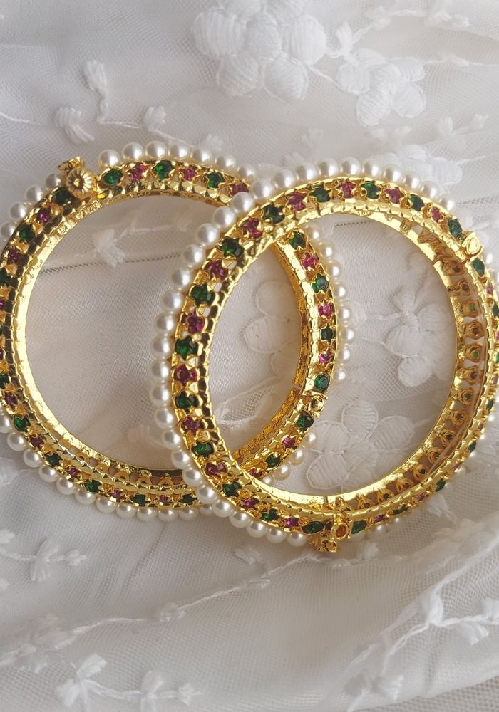 Multicolour Traditional Pearl Tode. Set of 2 gold-toned bangles adorned with pearls and colorful gemstones against a soft, floral background.