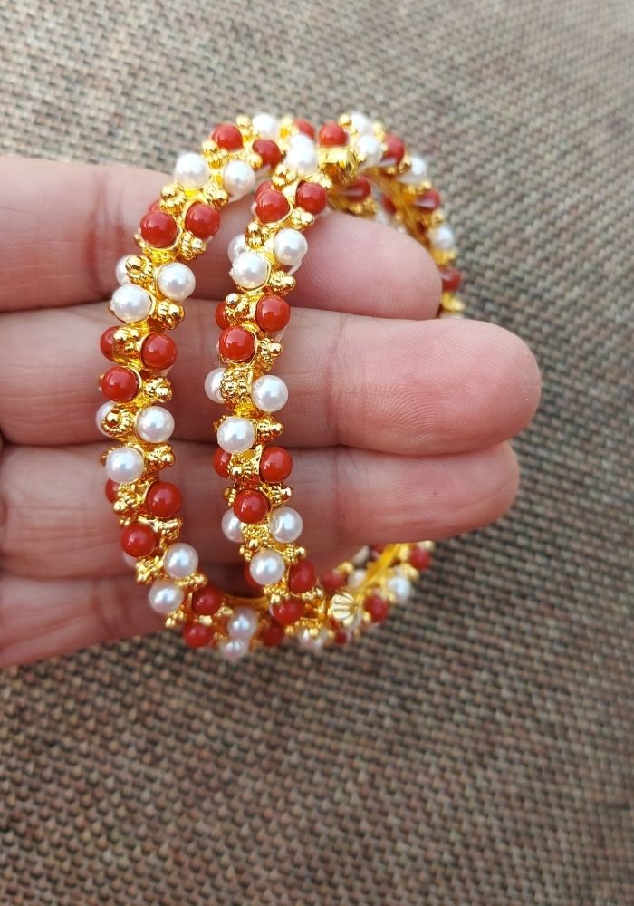 Decorative pearl and coral traditional Indian anklet with intricate golden design, held in hands.