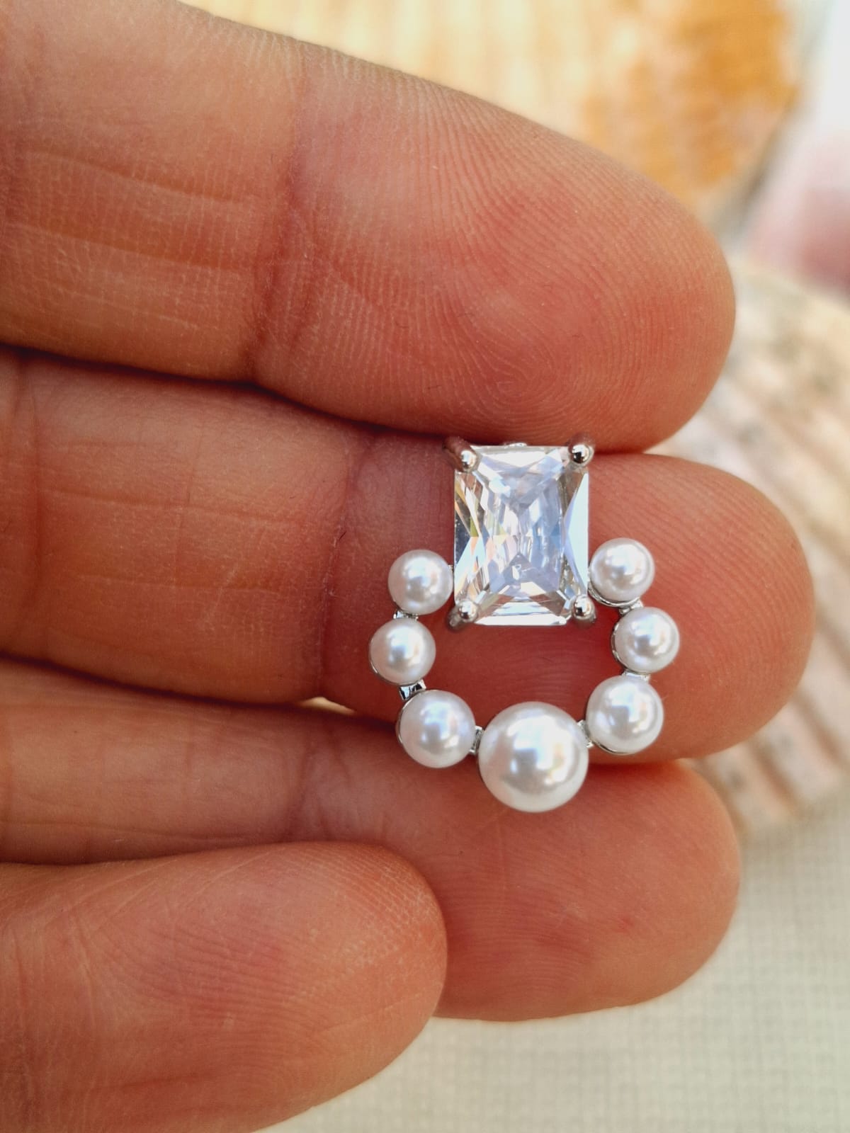 Elegant silver stud earrings with a central rectangular diamond and surrounding pearls, displayed against a soft background.