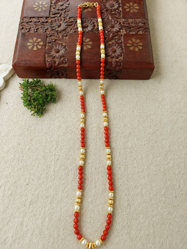 Exquisite coral and gold beaded necklace on a wooden floral patterned box, surrounded by a small sprig of greenery.