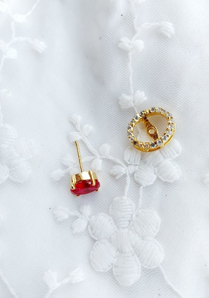 Elegant oval changeable gold-tone earrings with red and crystal accents displayed on a white floral background.