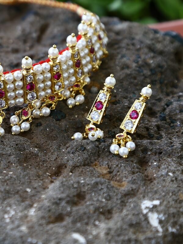 Ornate golden jewelry with pearl and ruby accents, placed on a rocky surface