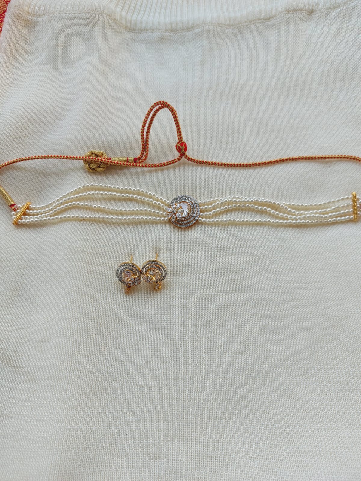 Elegant white and gold designer choker with floral accents, layered pearl strands, and stud earrings displayed on a white textile background.