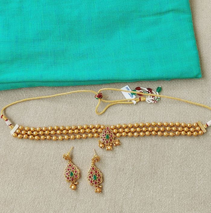Elegant gold and gemstone necklace and earrings set displayed on turquoise fabric background from Mugdha Jewellery Store