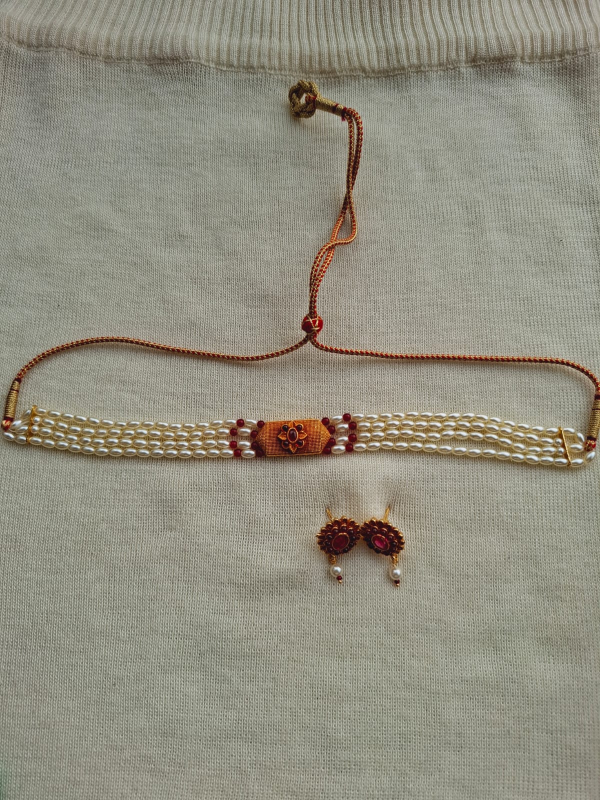 Elegant rice pearls geru designer choker with intricate floral accents, suspended on a metal hanger against a gray fabric background.