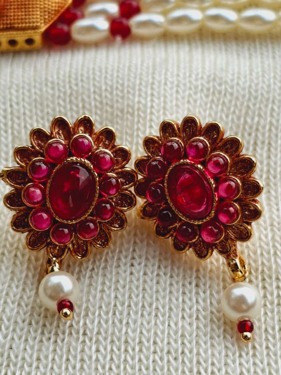 Elegant ruby-encrusted earrings from Mugdha Jewellery Store, displayed on a white knitted fabric background.