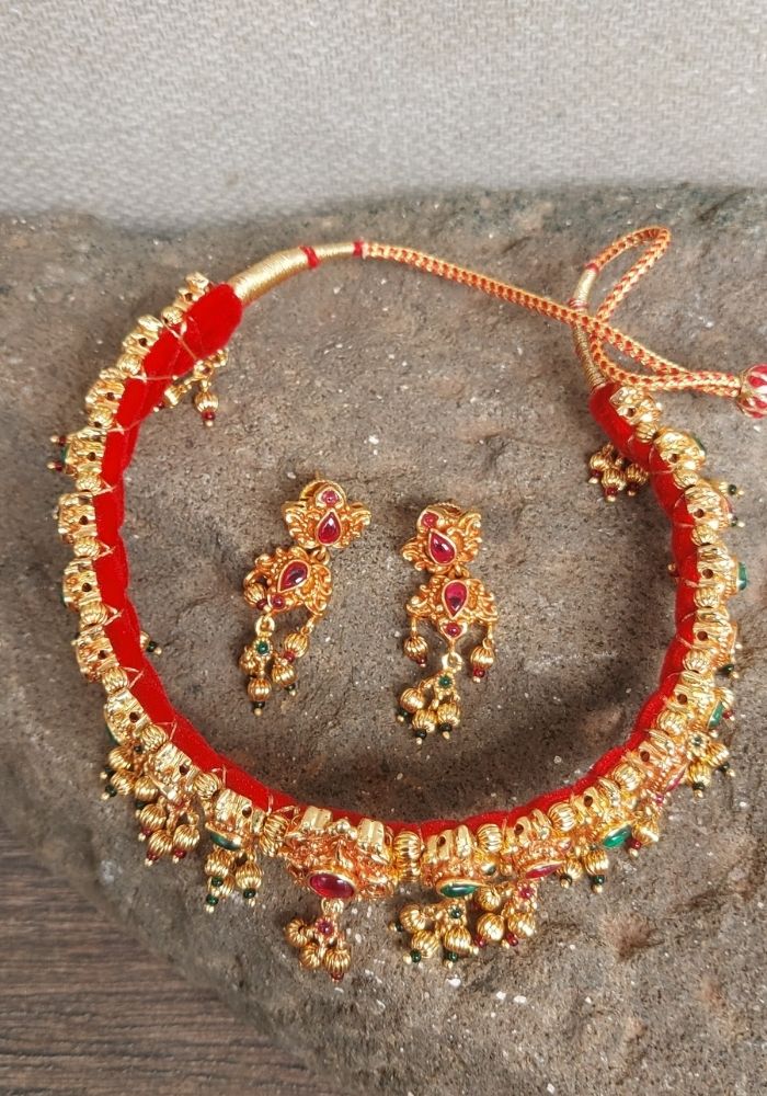 Elegant red and gold necklace and earrings set from Mugdha Jewellery Store. The necklace features a striking red thread with intricate gold detailing and ornaments. The matching earrings complement the necklace's design. This antique-style jewelry set showcases the brand's craftsmanship and attention to detail.