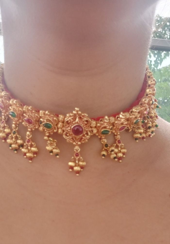 Intricate antique gold necklace with floral motifs and dangling gems, showcased on a woman's neck in the Mugdha Jewellery Store product image.