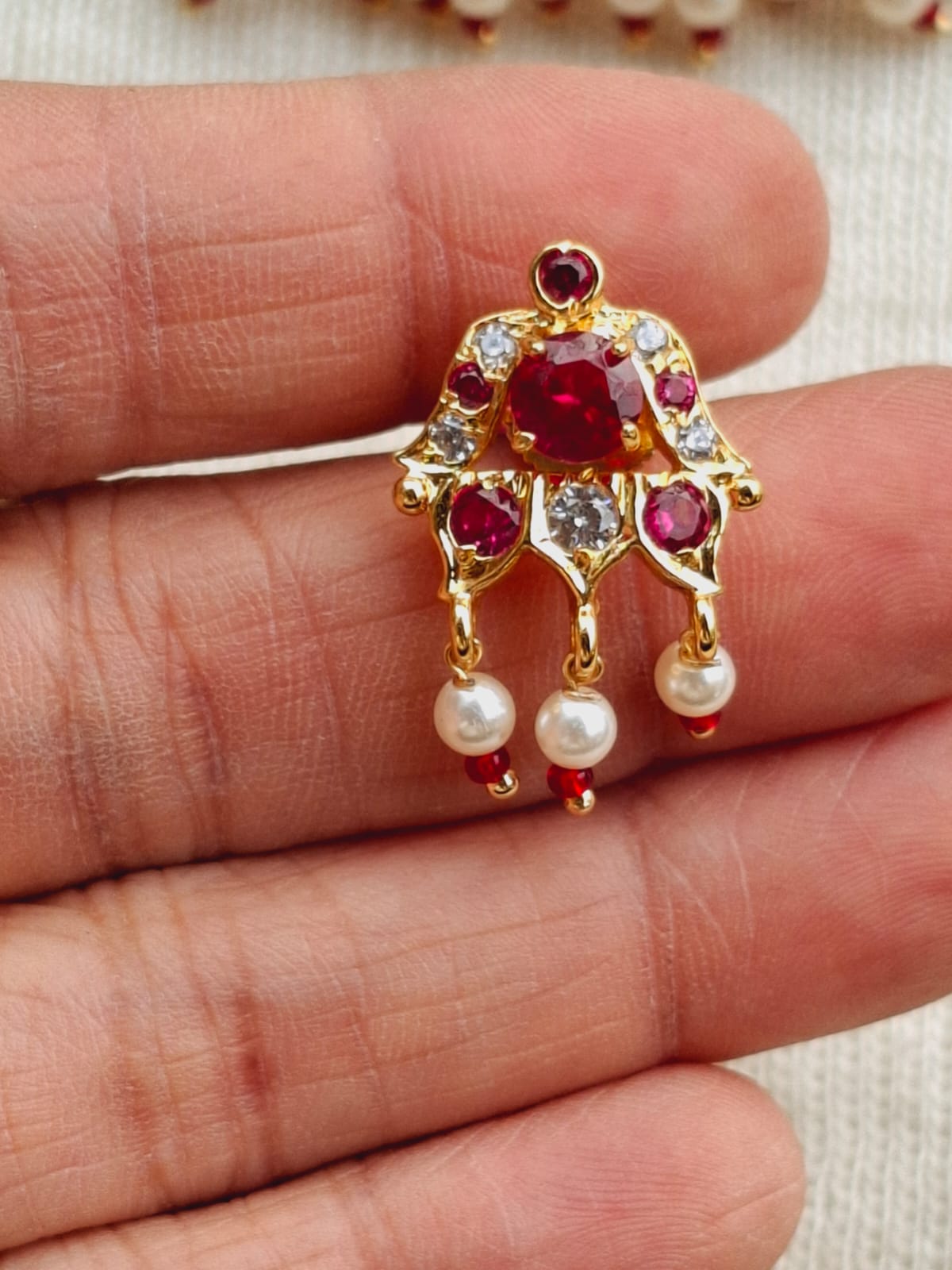 Elegant gold-toned choker pendant with vibrant red and white gemstones, featuring hanging pearl accents, displayed on a human hand.