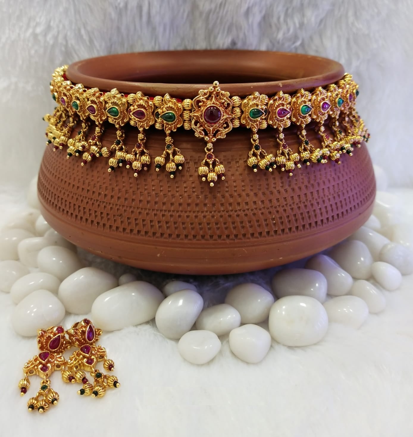 Royal Antique Gadi Chinchpeti: Ornate gold-toned jewelry set displayed in a clay pot, surrounded by white pebbles.
